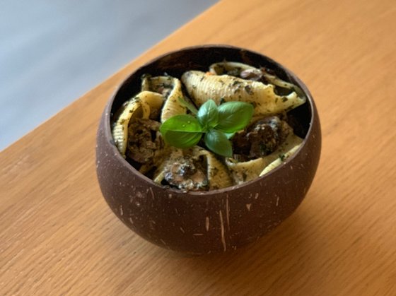 Lumaconi Giganti pasta bowl with garlic, mushroom, and kale, topped with vegan cheesy sauce